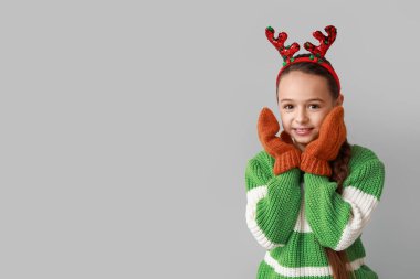 Gri arka planda ren geyiği boynuzları olan tatlı küçük bir kız.