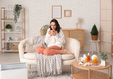 Evdeki kanepede oturan bir fincan çayla hasta genç kadın.