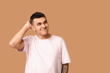 Kahverengi arka planda yakışıklı, utangaç genç bir adam.