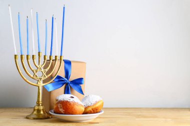 Lezzetli donutlar, menorah ve Hanuka kutlaması için tahta masada hafif arka planda bir tabak.