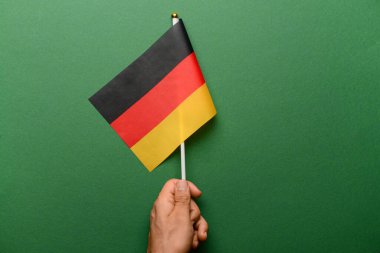 Yeşil arka planda Almanya bayrağı taşıyan bir erkek.