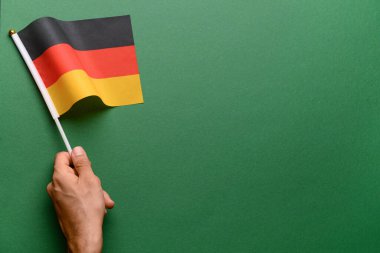 Yeşil arka planda Almanya bayrağı taşıyan bir erkek.