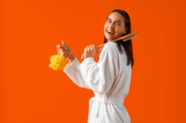 Üzerinde banyo lifi ve turuncu arka planda masaj fırçası olan genç bir kadın.