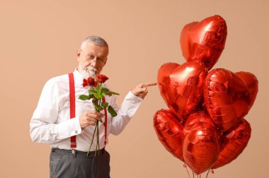 Elinde gül çiçekleri olan olgun bir adam bej arka planda kalp şeklinde balonlara bakıyor. Sevgililer Günü kutlaması