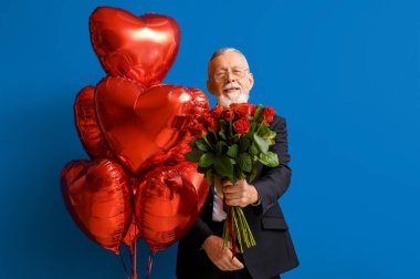 Mavi arka planda gül buketi ve kalp şeklinde hava balonları olan olgun bir adam. Sevgililer Günü kutlaması