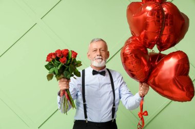 Yeşil arka planda gül buketi ve kalp şeklinde hava balonları olan olgun bir adam. Sevgililer Günü kutlaması