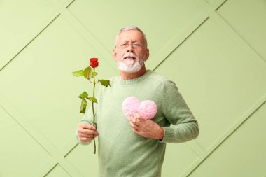 Yeşil arka planda Sevgililer Günü için gül çiçeği ve kumaştan kalbi olan olgun bir adam.