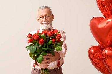 Beyaz arka planda Sevgililer Günü için çiçek buketi ve kalp şeklinde hava balonları olan olgun bir adam.