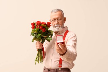 Olgun bir adam elinde gül buketi ve beyaz arka planda nişan yüzüğü olan bir kutu tutuyor. Sevgililer Günü kutlaması