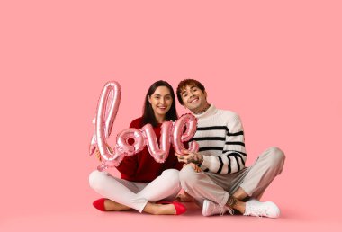 Pembe arka planda aşk kelimesi şeklinde balonları olan genç bir çift. Sevgililer Günü kutlaması