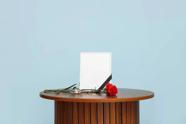 Blank funeral frame, burning candle and carnation flower near color wall