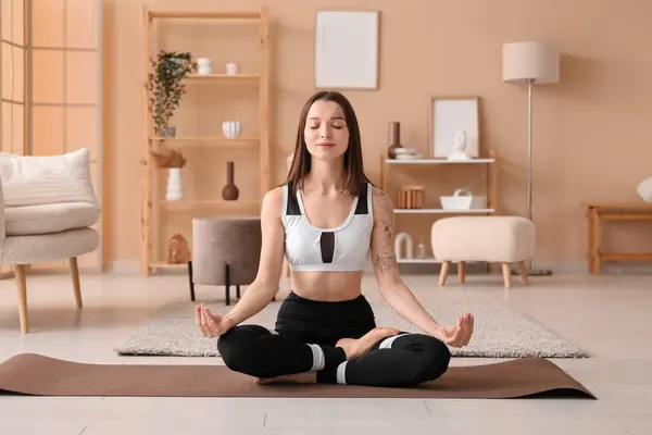 Stock image Sporty young woman meditating on mat at home