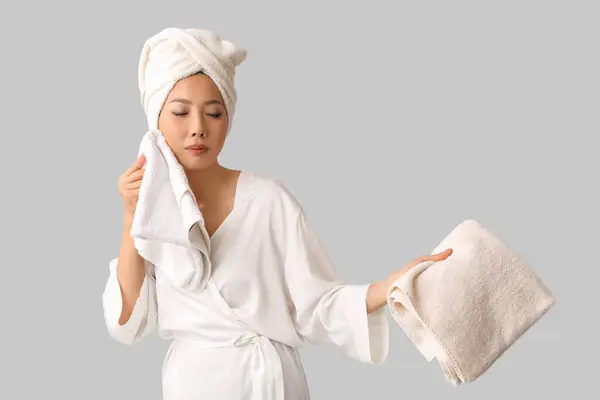 Young Asian woman in gown with clean towels after shower on light background