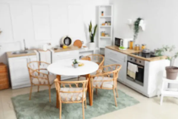 Blurred view of light kitchen with green plants, counters and dining table