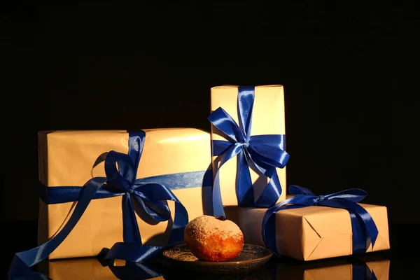 Gifts for Hanukkah celebration and tasty donut on dark background