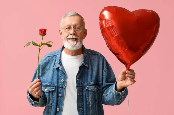 Mature man with rose flower and air balloon in shape of heart on pink background. Valentine\'s day celebration
