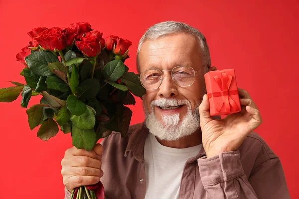 Mature man with bouquet of roses and gift for Valentine\'s day on red background