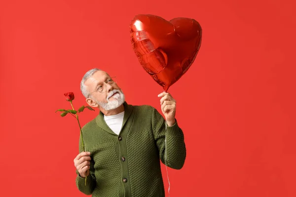 Mature man with rose flower and air balloon in shape of heart for Valentine\'s day on red background