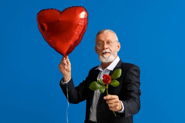 Mature man with rose flower and air balloon in shape of heart on blue background. Valentine\'s day celebration