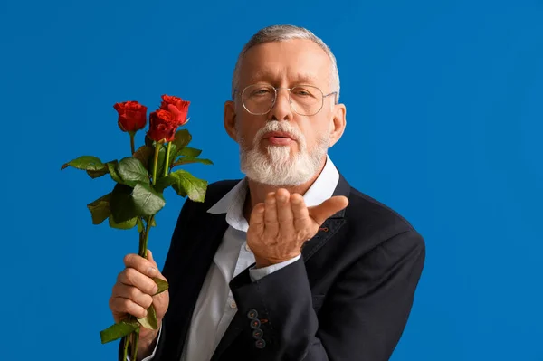 Mature man with rose flowers blowing kiss on blue background. Valentine\'s day celebration