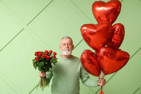 Mature man with bouquet of roses and air balloons in shape of heart for Valentine\'s day on green background