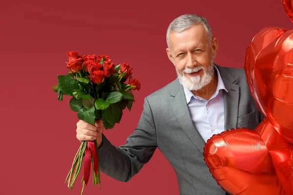 Mature man with bouquet of roses and air balloons in shape of heart for Valentine's day on red background