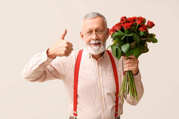 Mature man with bouquet of roses showing thumb-up on white background. Valentine\'s day celebration