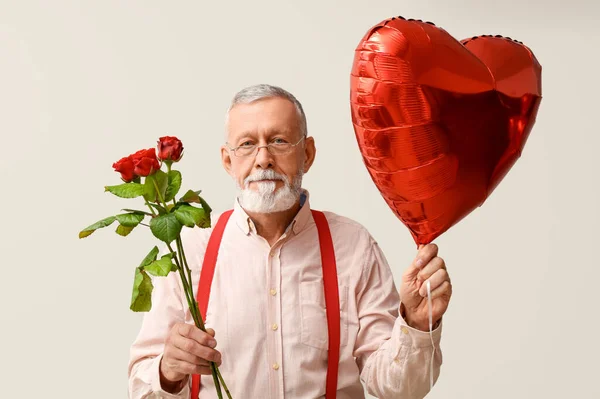 Mature man with rose flowers and air balloon in shape of heart on white background. Valentine\'s day celebration