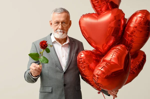 Mature man with rose flower and air balloons in shape of heart on white background. Valentine\'s day celebration