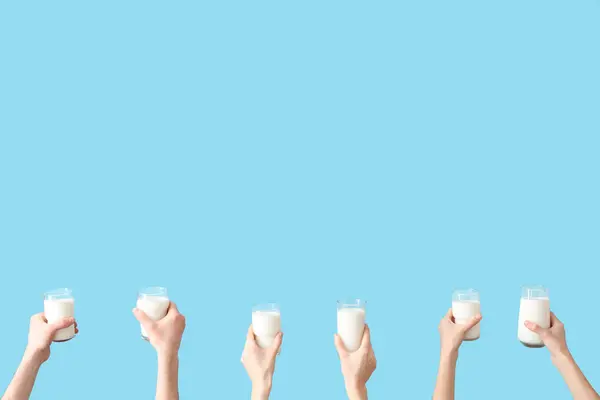 Hands with glasses of milk on blue background