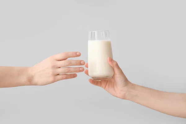 Hands handing over glass of milk on grey background