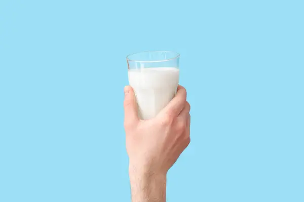 Hand with glass of milk on blue background