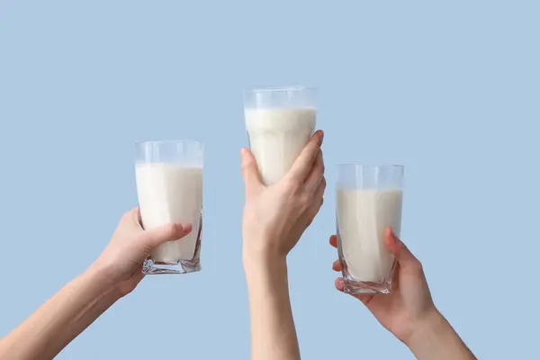 Hands with glasses of milk on light blue background