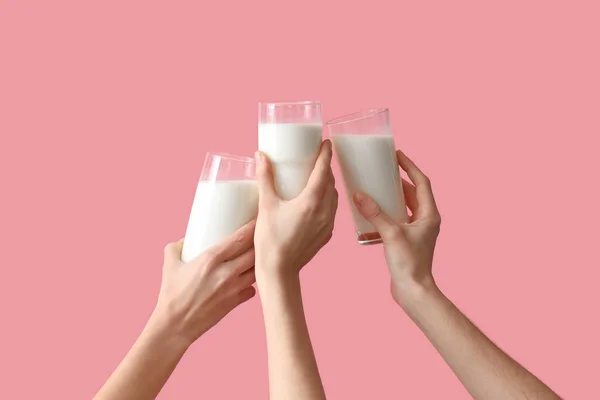 Hands clinking glasses of milk on pink background