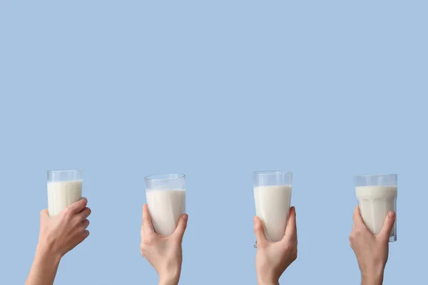Hands with glasses of milk on light blue background