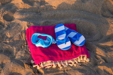 Şnorkelli maske, parmak arası terlikler ve deniz sahilinde renkli bir havlu.