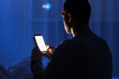 Genç adam gece yatağında cep telefonu kullanıyor, yakın plan.