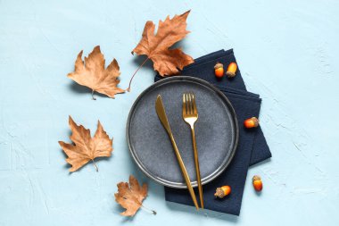 Kuru akçaağaç yaprakları ve mavi arka planda meşe palamudu ile süslü sonbahar masası ayarları