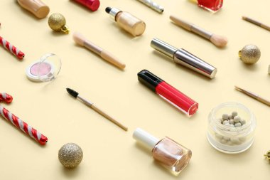 Farklı dekoratif kozmetik ürünleri, sarı arka planda Noel topları ve şeker kamışları.