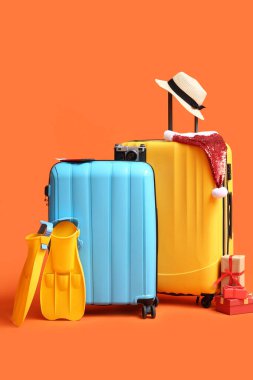 Plaj aksesuarlı bavullar, Noel Baba şapkası ve renk arkaplanlı Noel hediyeleri.