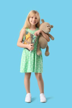 Pelüş oyuncak ayısı ve mavi arka planda peri masalı kitabı olan şirin bir kız.