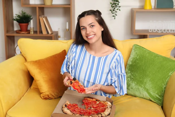 Beautiful young woman with tasty pizza sitting on sofa at home