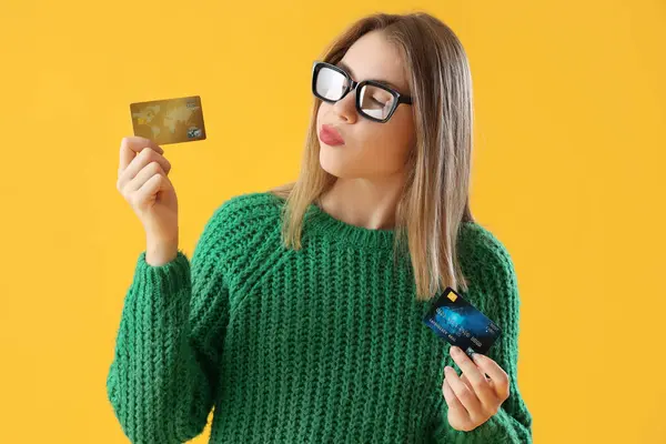 Thoughtful young woman with credit cards on yellow background