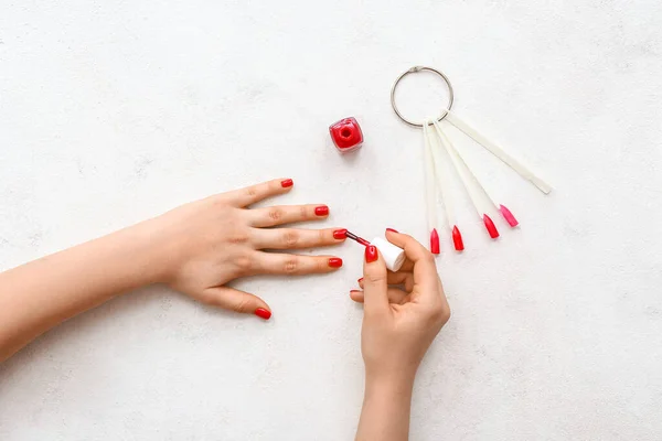 Woman painting her nails with red polish on white grunge background