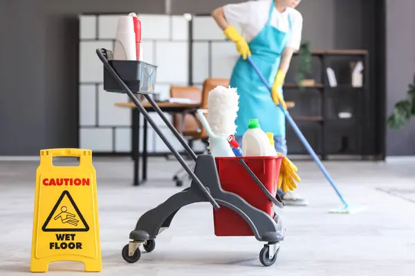 Trolley with cleaning supplies and caution sign in office