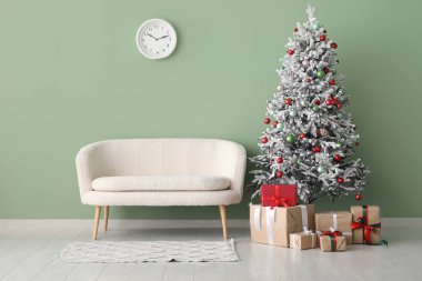 Yeşil duvara karşı hediyeler ve kanepe ile süslenmiş Noel ağacı.