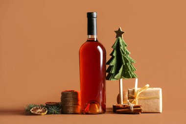 Bir şişe şarap ve Noel ağacı, tarçın, kurutulmuş portakal ve kahverengi arka planda hediye kutusu.