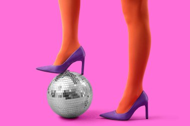 Pembe arka planda disko topu olan şık topuklu ayakkabılı bir kadın.