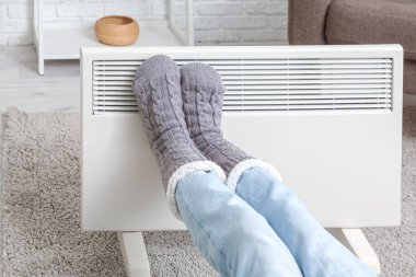 Elektrikli ısıtıcının yanında sıcak kış çorapları giymiş genç bir kadın. Isınma mevsimi kavramı