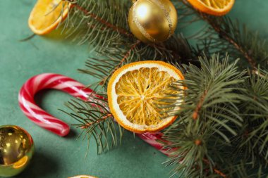 Kurumuş portakal dilimleri, şeker kamışı, köknar dalları ve yeşil arka planda Noel topları.